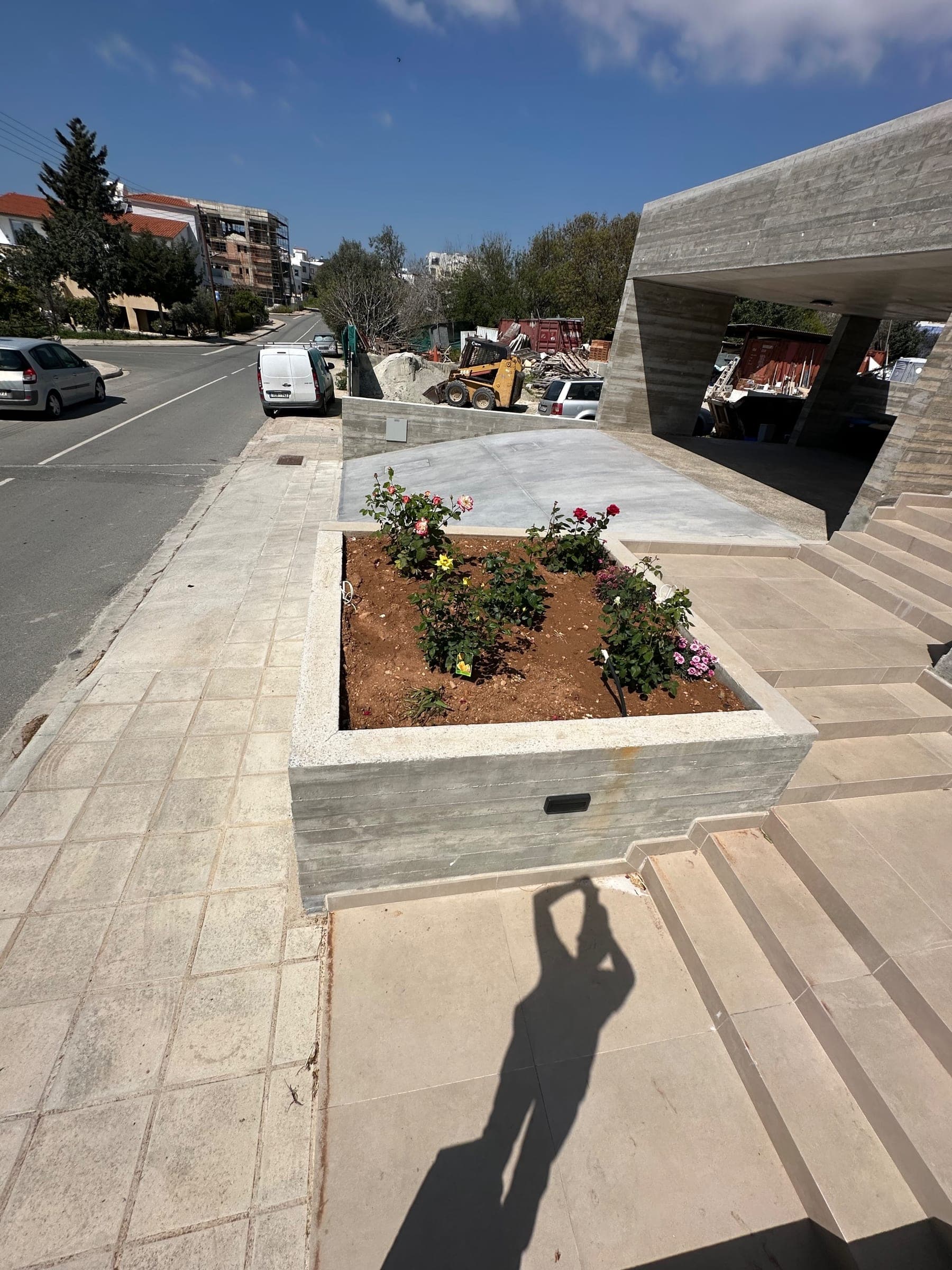 Modern concrete raised planter bed with flowering plants and shrubs on paved courtyard with contemporary architectural elements.