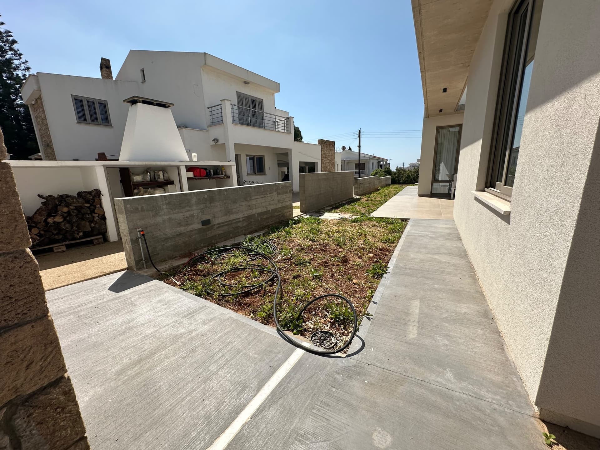 Modern garden pathway with concrete paving, young planted beds, irrigation lines, and white contemporary residential buildings with stone walls.